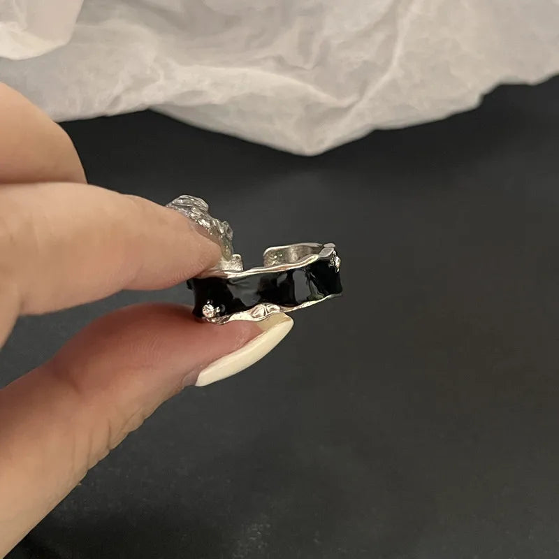 Bague argentée avec émail noir et motif tête de mort, tenue entre les doigts