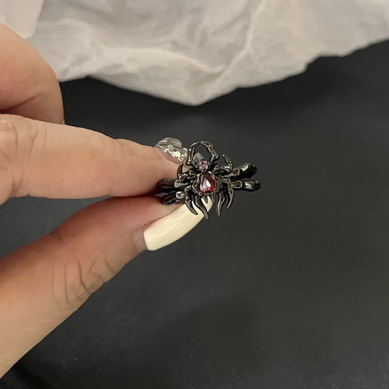 Bague araignée noire avec pierre rouge, tenue entre les doigts