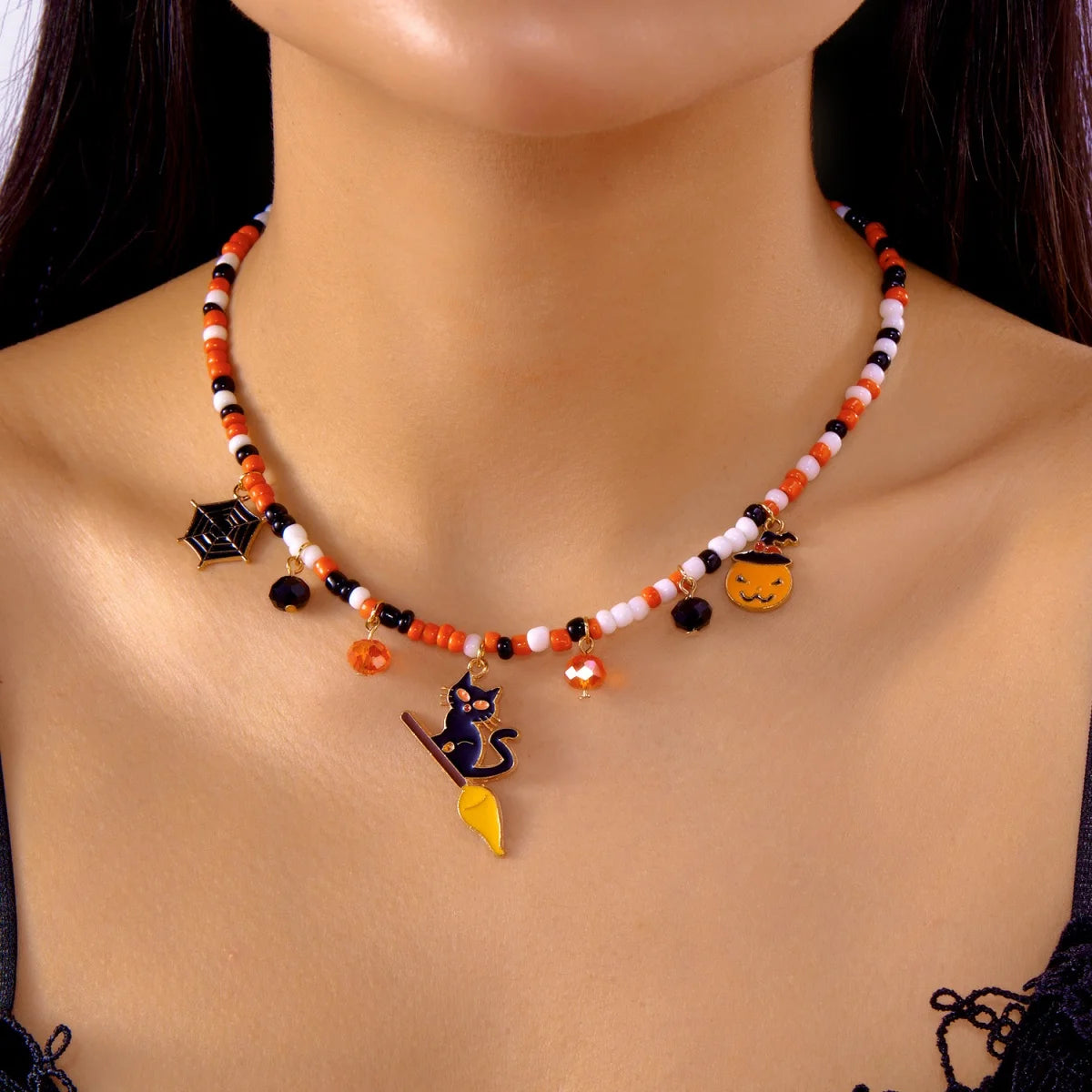 Collier Halloween en perles orange, blanches et noires avec pendentifs toile d'araignée, chat noir et citrouille, porté autour du cou