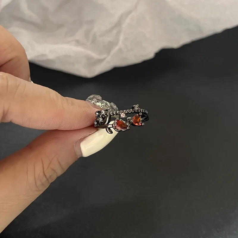 Bague en métal sombre avec pierres cœur rouges, tenue entre les doigts