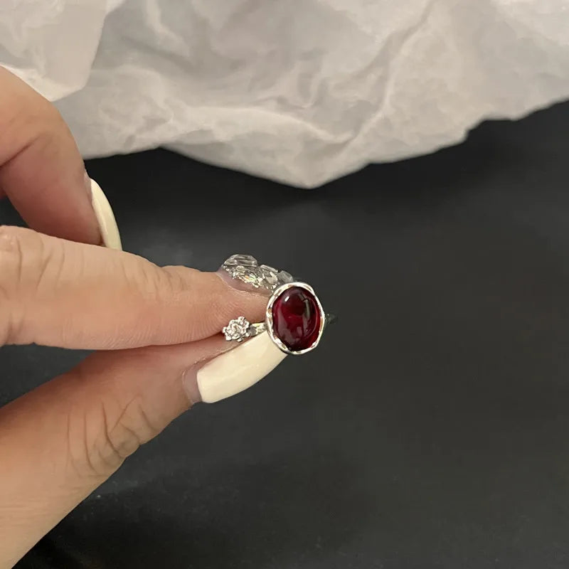 Bague argentée avec pierre ovale rouge, tenue entre les doigts