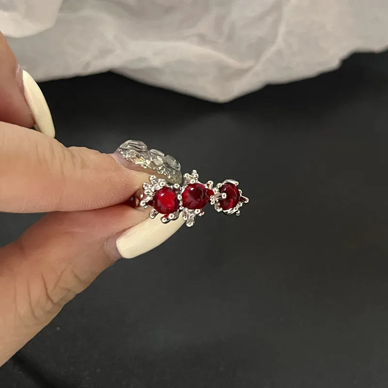 Bague argentée avec trois pierres rondes rouges, tenue entre les doigts