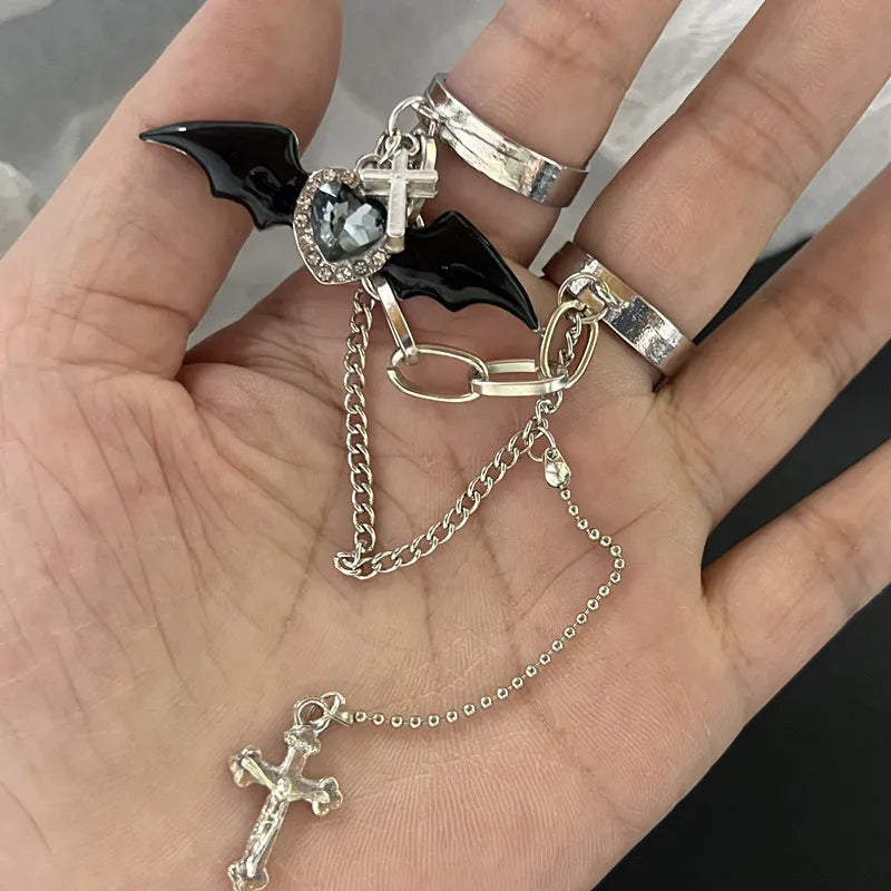 Main portant des bagues gothiques avec ailes de chauve-souris, cœur et croix, reliées par une chaîne