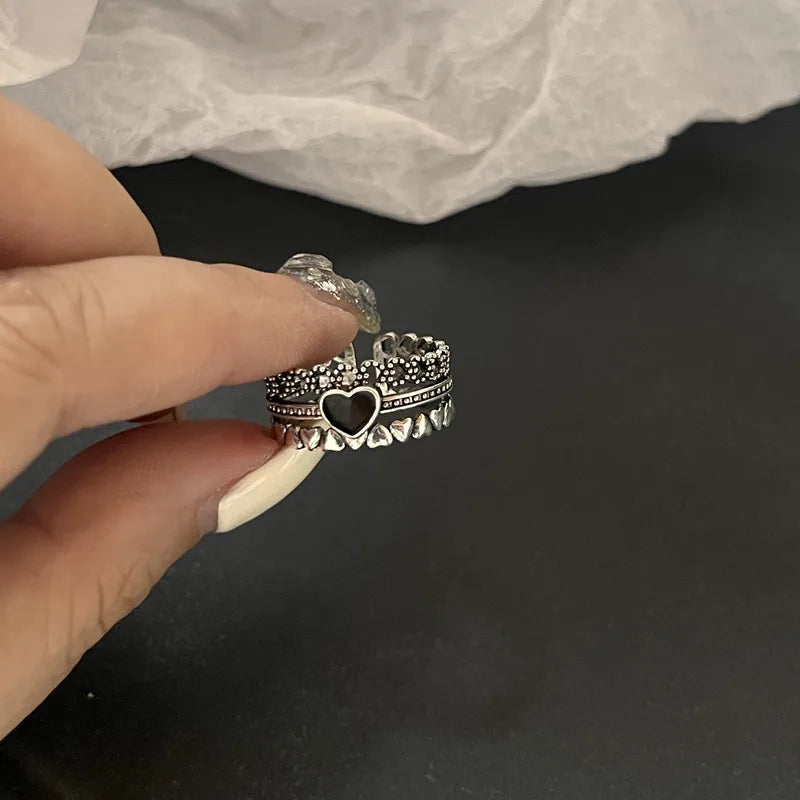 Bague argentée avec pierre cœur noire, tenue entre les doigts